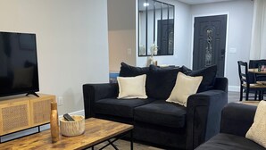 A modern living room with a black sofa, a wooden coffee table, and a TV on a stand. - Your Forever Home (Lutz)