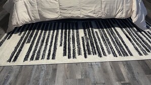 A bedroom with a large bed, two nightstands, a black and white striped rug, and a framed picture on the wall. - Your Forever Home (Lutz)