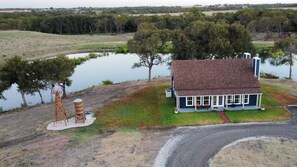 A house with a porch and a small pond in the background. - Doe's Hideaway - rural retreat (Riesel)