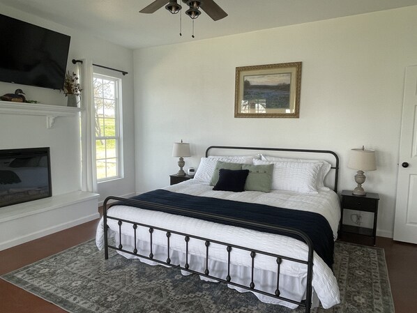 A bedroom with a bed, two bedside tables, a nightstand, a fireplace, and a painting on the wall. - Doe's Hideaway - rural retreat (Riesel)
