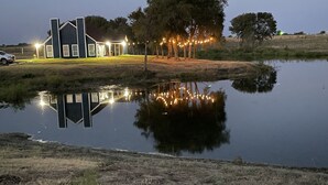 Uma casa com lago à frente, cercada por árvores e gramado.