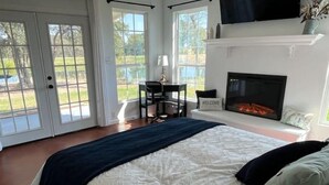 Quarto com uma cama grande, lareira e vista através de portas francesas.