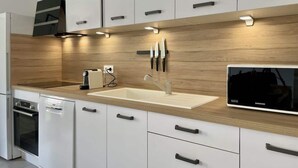 A modern kitchen with white cabinets, a wooden countertop, a built-in sink, and a Samsung TV. - Alba (Laxou)