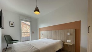 A modern bedroom with a large bed, a green chair, a bedside table, and a window with a view. - Alba (Laxou)