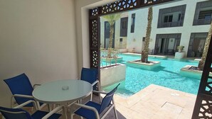 Une pièce avec une table en verre et des chaises bleues, une piscine et une vue sur un immeuble doté de balcons.