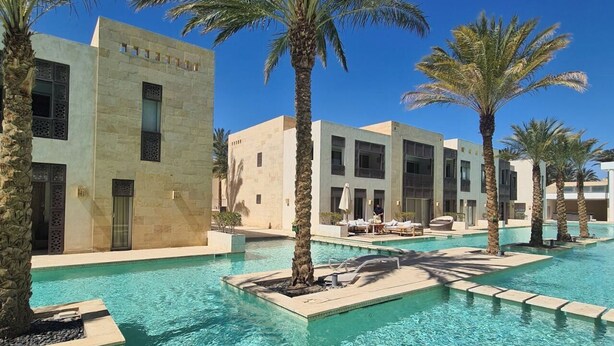 Un espace piscine avec une eau cristalline, des palmiers et des bâtiments modernes dotés de balcons.