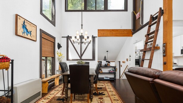 A spacious living room with a large brown leather sofa, a dining area with a wooden table and chairs, and a kitchen in the background.