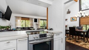 A modern kitchen with white cabinetry, a built-in stove, and a dining area with a table and chairs.