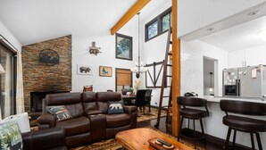 A modern living room with a fireplace, leather sofa, wooden coffee table, and a kitchen area with bar stools.