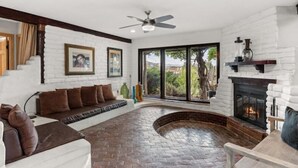 A cozy living room with a fireplace, a stone floor, and a large window offering a view of the outdoors.