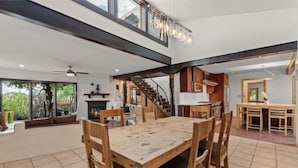 A spacious dining area with a wooden table and chairs, a staircase leading to an upper level, and a view of the outdoors through large windows.
