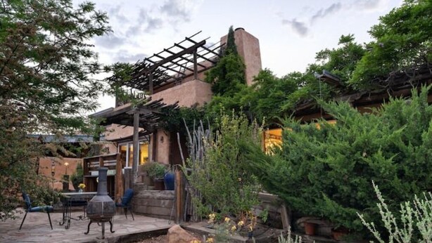 A rustic outdoor patio with a pergola, stone steps, and a variety of plants.