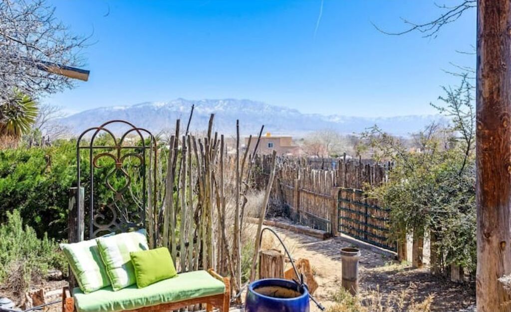 Un espace extérieur aménagé dans un style rustique, avec une clôture en bois, un portail en métal et une vue sur les montagnes en arrière-plan.