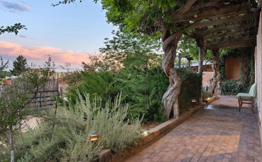 Ein Garten mit einer Patio, einem Pergola, verschiedenen Pflanzen und einem Pflasterweg.