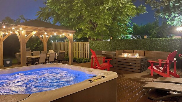 Ein Whirlpool mit einer Holzterrasse, roten Stühlen und einem überdachten Sitzbereich mit Lichterketten.