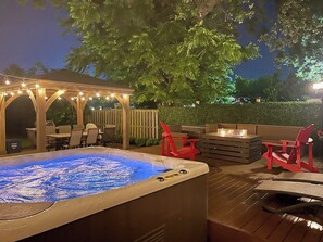 Un bain à remous avec une terrasse en bois, des chaises rouges et un espace salon couvert agrémenté de guirlandes lumineuses.