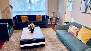Ein Wohnzimmer mit einem grünen Sofa, einem blauen Sofa, einem Couchtisch mit Blumen und einer Lampe.