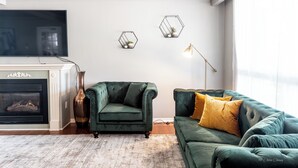 Ein Wohnzimmer mit Kamin, zwei grüne Sofas, einem großen Flachbildfernseher und zwei sechseckigen Wanddekorationen.