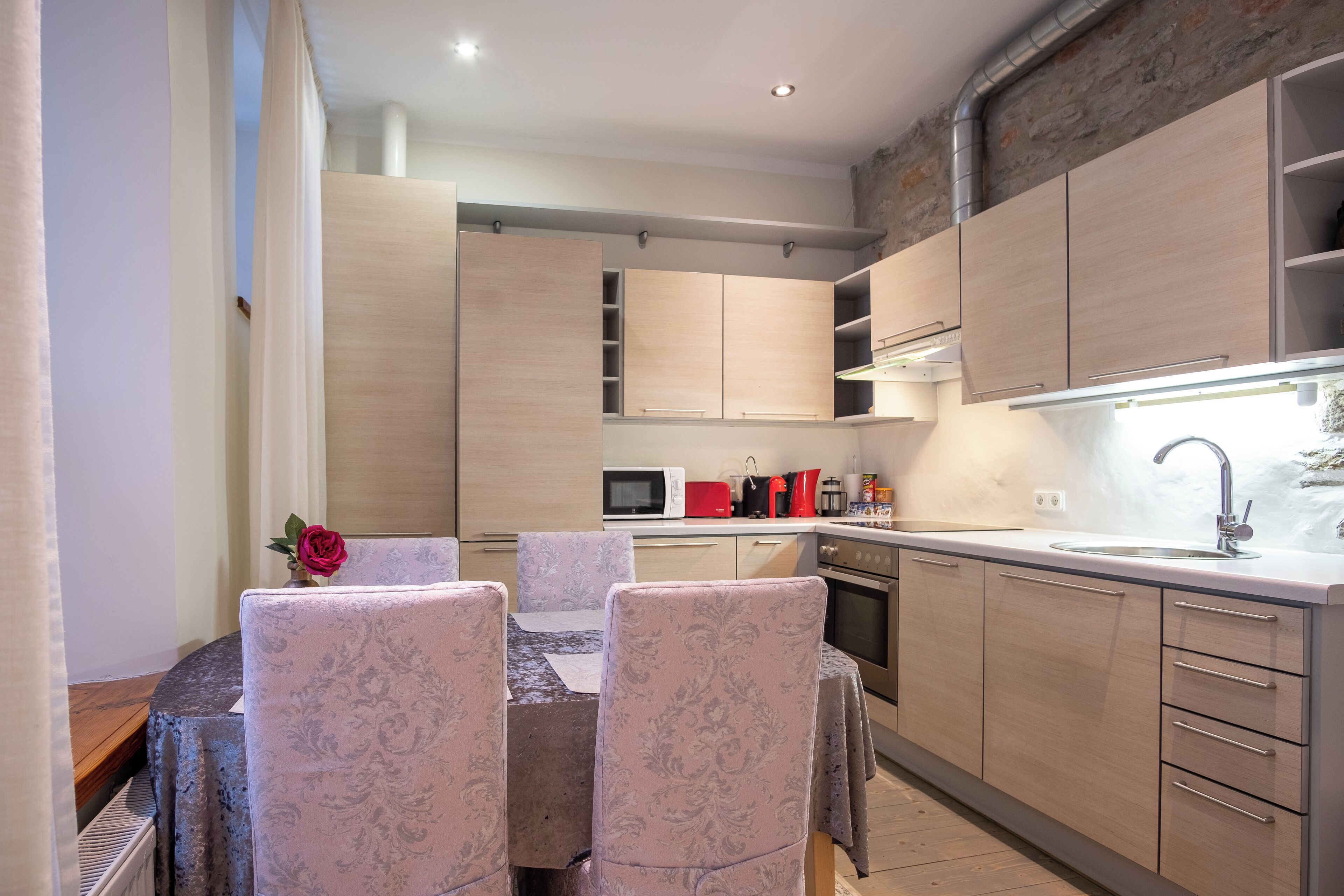 A modern kitchen with wooden cabinets, a dining table with patterned chairs, and a built-in microwave.