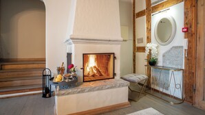 Ein Kamin mit Feuer, eine Bank und ein Konsolentisch mit Spiegel und Blumen.