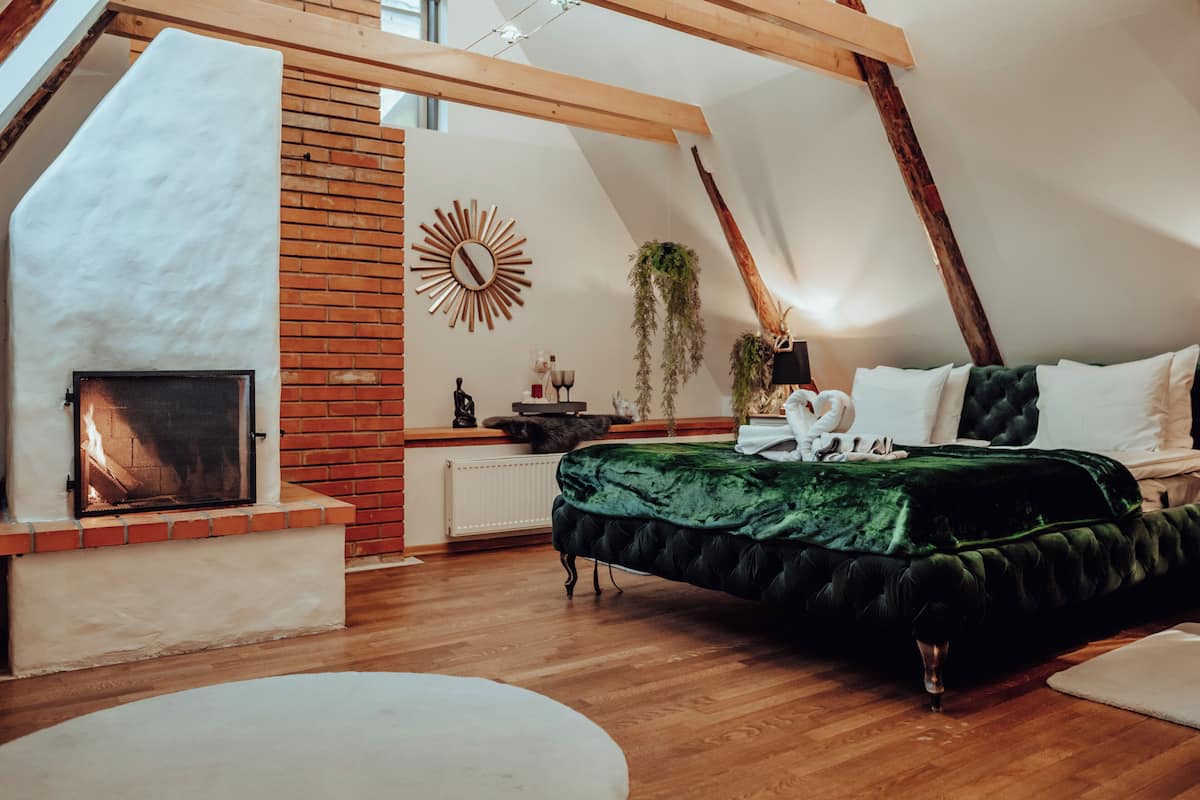 Ein Schlafzimmer mit schrägen Wänden, einem Kamin, einem Bett mit grüner Samtdecke und Holzboden.