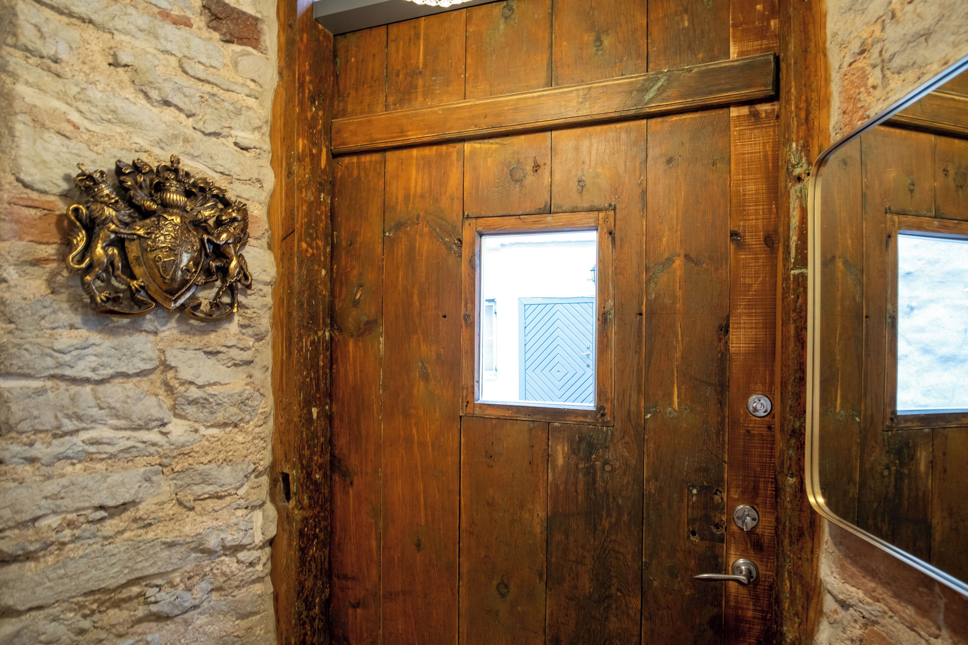 Eine Holztür mit kleinem Fenster und einem Wappen an der Wand.
