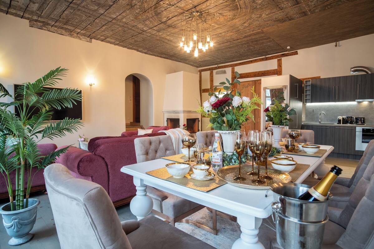Ein modernes Wohnzimmer mit Esstisch, gedecktem Tisch für eine Mahlzeit, Kamin und Küchenbereich.