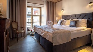 Ein Schlafzimmer mit einem großen Bett, einem Holzstuhl, einem Fenster mit Vorhängen und einer Wandlampe.