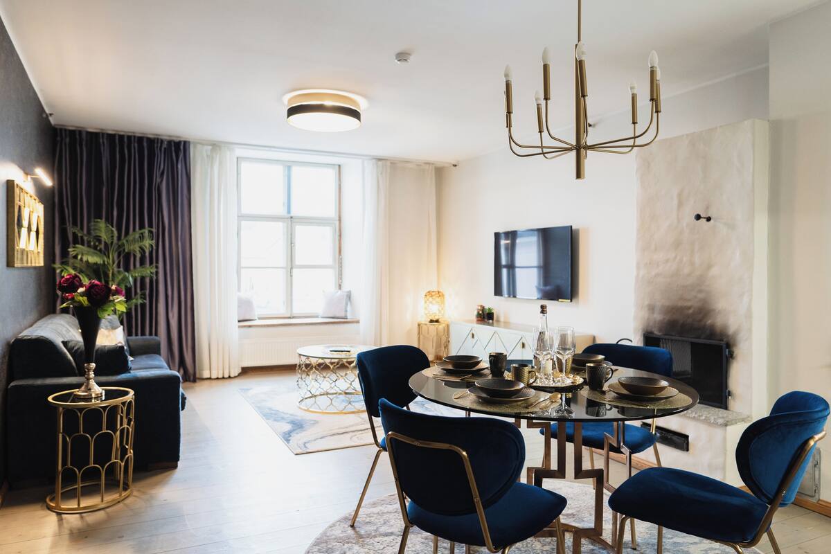 Ein modernes Wohnzimmer mit einem runden Esstisch, blauen Polsterstühlen, einer Couch und einem Kamin.