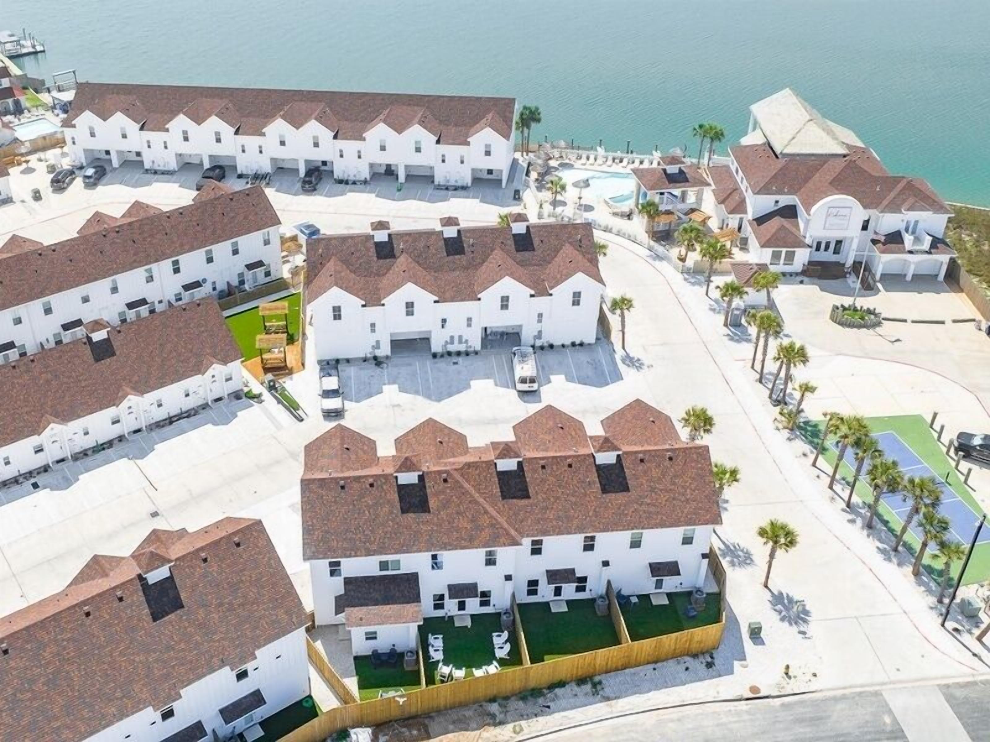 Una zona residencial costera con casas blancas, una piscina y una cancha de tenis.