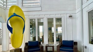 A room with wicker furniture, a yellow abstract sculpture, and large windows. - A Wave From it All (Corpus Christi)