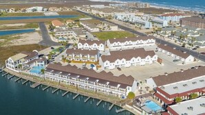 An aerial view of a coastal resort with multiple buildings, a marina, and a beach. - A Wave From it All (Corpus Christi)