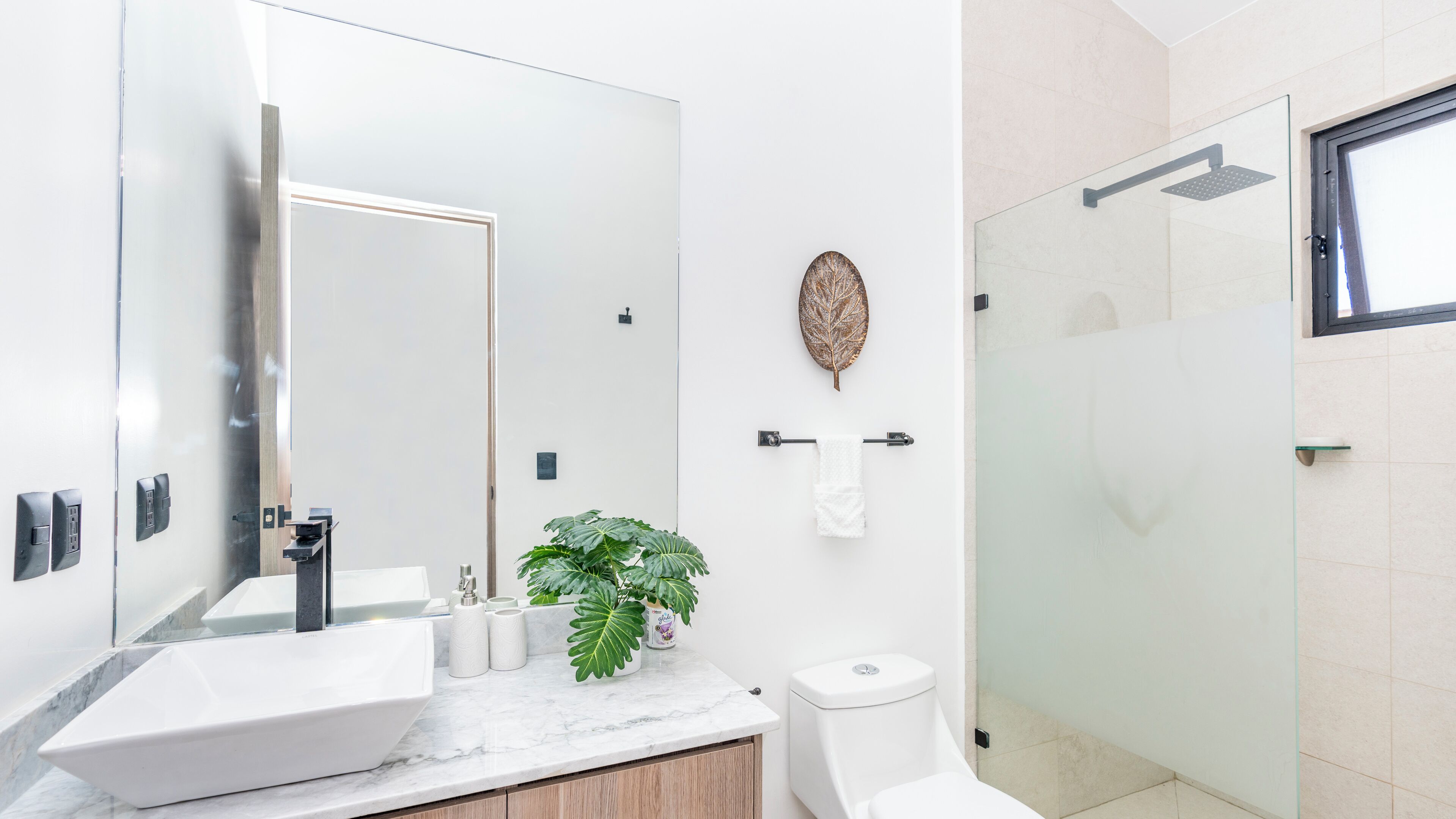 Ein modernes Badezimmer mit großem Spiegel, Waschbecken in Weiß, Toilette und Duschkabine aus Glas.