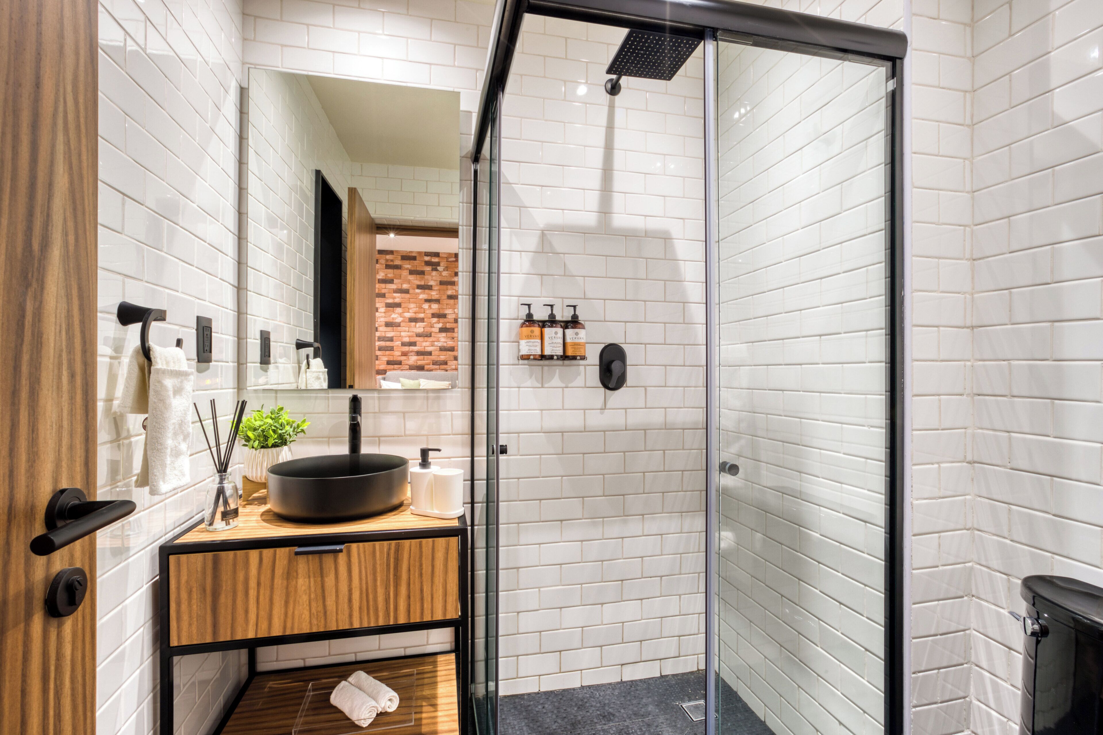A modern bathroom with a large mirror, a black sink, wooden vanity, and a glass shower enclosure.