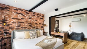 Een moderne slaapkamer met een metselwerk muur, een groot bed met veel kussens, een nachtkastje met een lamp en een bureau met een stoel.