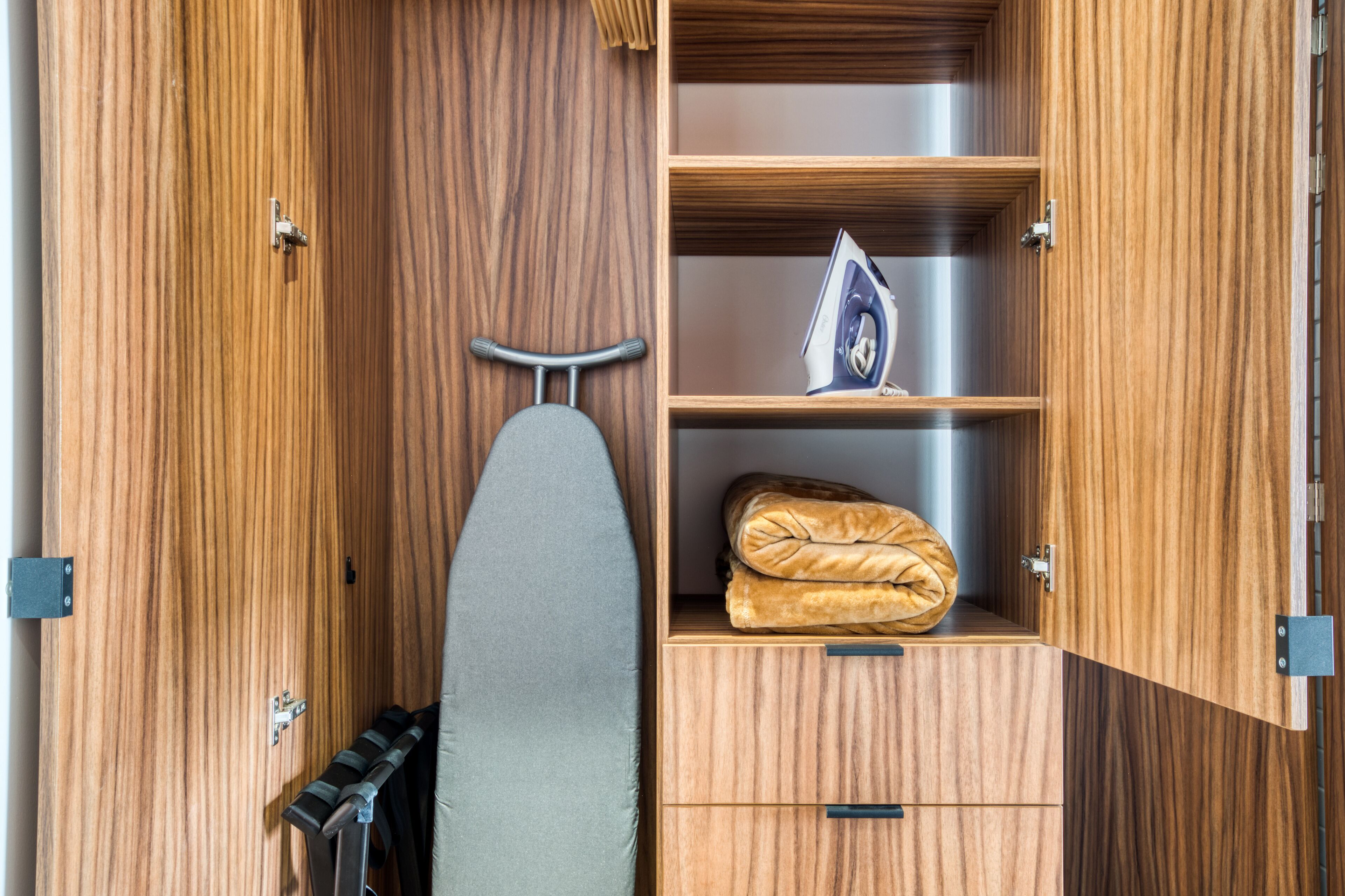 A wooden wardrobe with a hanging iron, an ironing board, and a folded blanket.