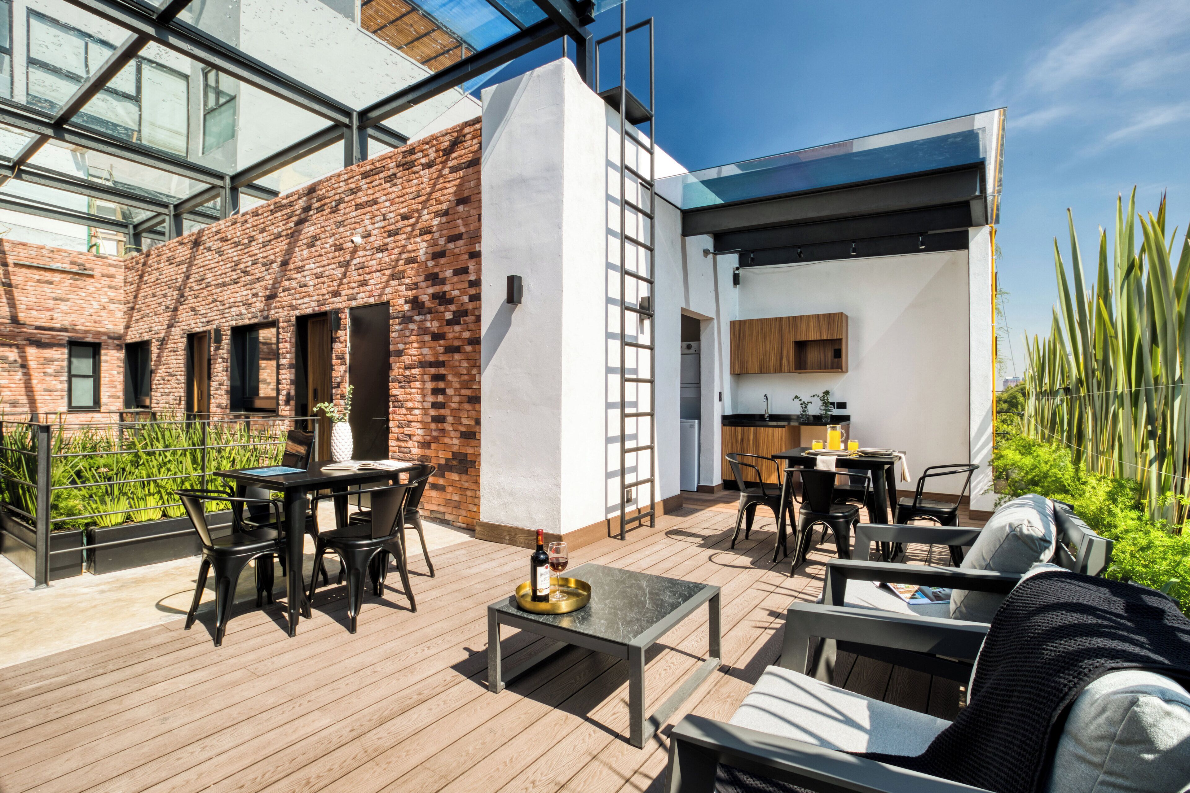 A modern outdoor patio with wooden flooring, black furniture, and a brick wall.