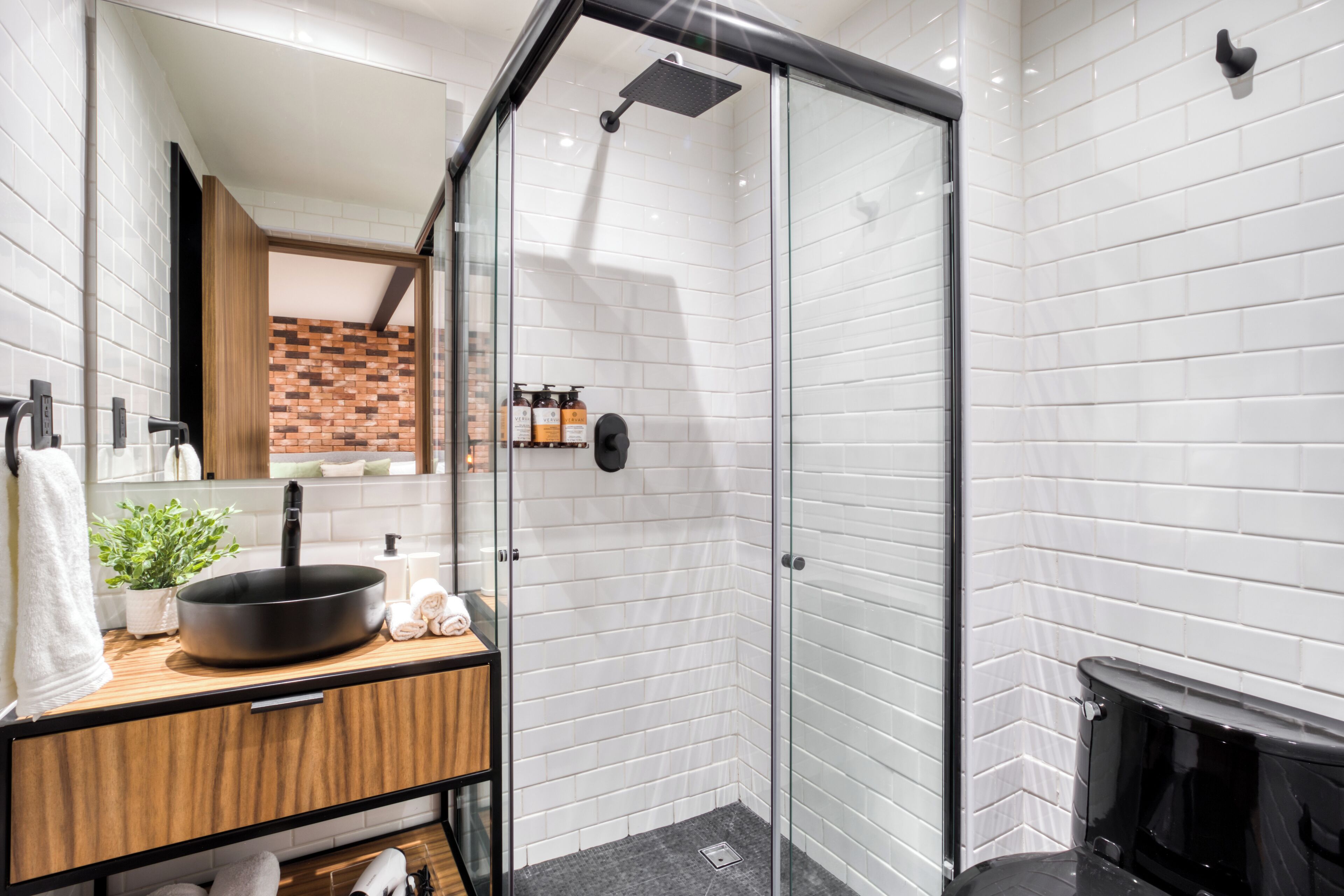 A modern bathroom with a glass-enclosed shower, white subway tiles, a wooden vanity, and a black sink.