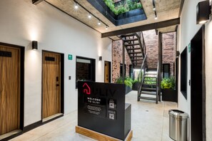 A modern interior with a welcome sign, wooden doors, a staircase, and a trash bin. - ULIV Roma Norte (Mexico City)