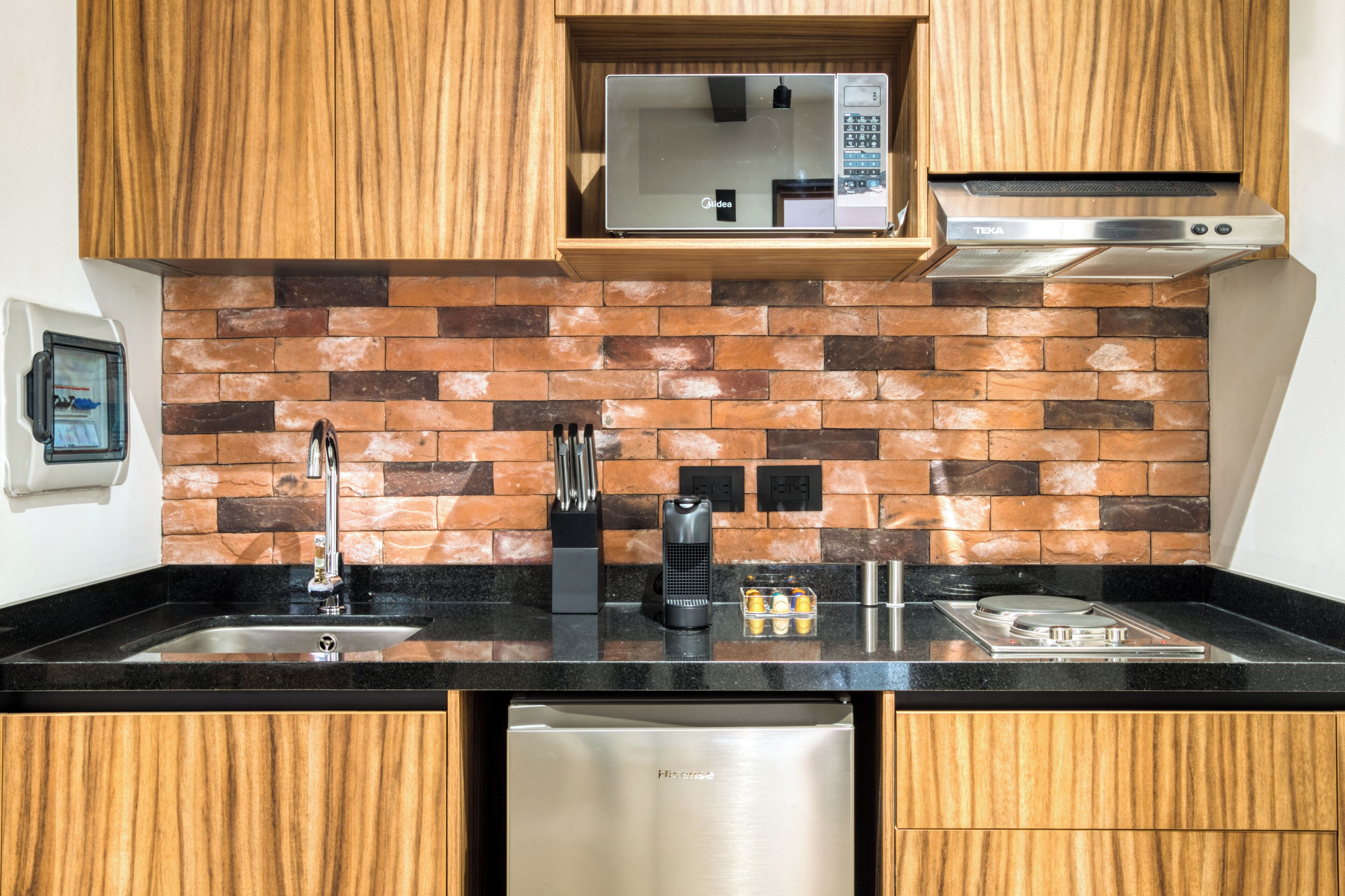 Una cocina con armarios de madera, salpicadero de ladrillo, refrigerador de acero inoxidable, microondas y estufa a gas.