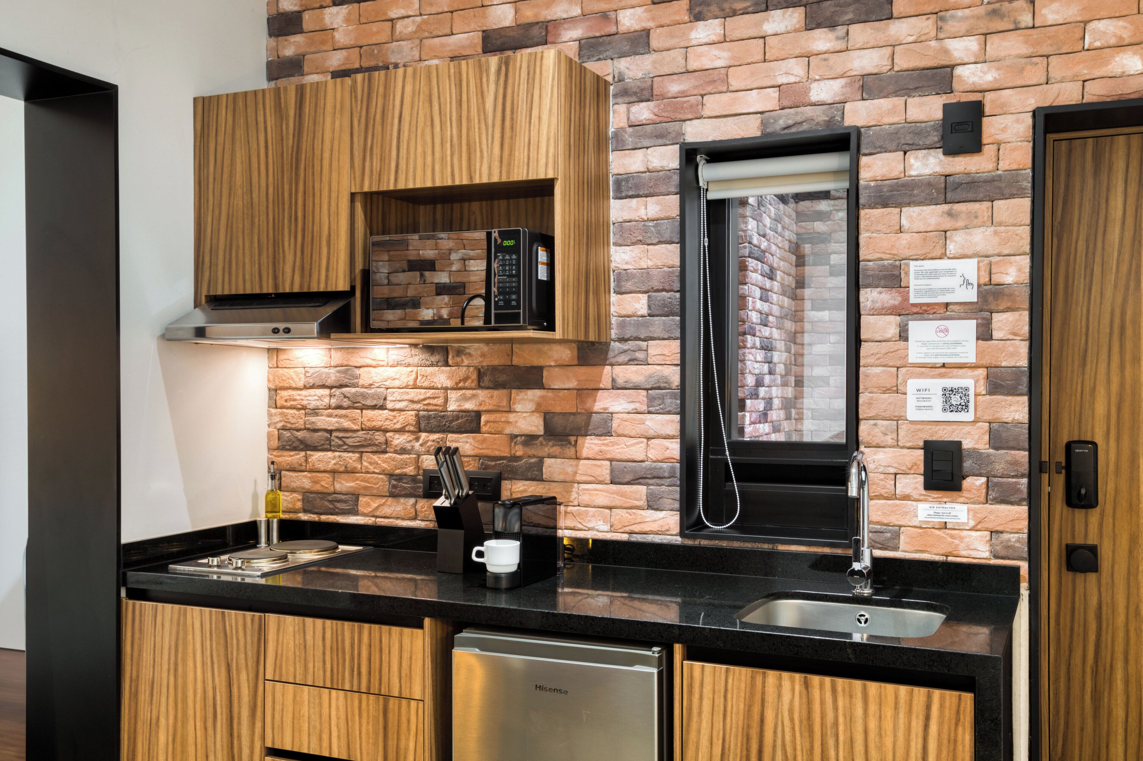 A modern kitchen with a brick wall, wooden cabinets, a built-in microwave, and a sink.