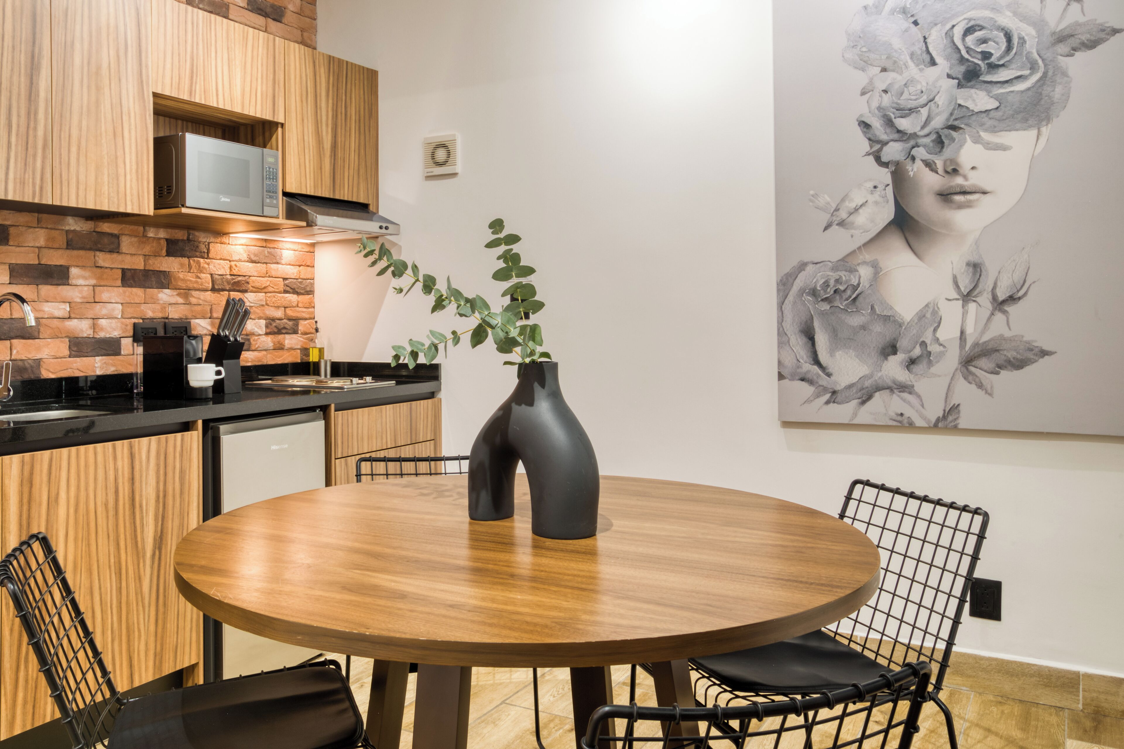 Eine moderne Küche mit Holzschränken, einer Mikrowelle und einem Essbereich mit einem runden Holztisch und schwarzen Stühlen.