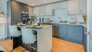 Eine moderne Küche mit grauen Schränken, einer zentralen Kochinsel mit Sitzgelegenheiten und einem eingebauten Backofen.