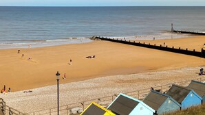 Ein Strand mit sandigem Ufer, einem steinernen Wellenbrecher und mehreren kleinen, blauen Gebäuden.