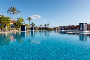 Ein klares Schwimmbecken mit Liegestühlen und Palmen, umgeben von Gebäuden.