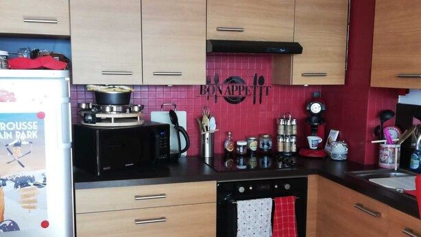 Una cocina compacta con armarios de madera, una estufa negra y un salpicadero rojo.