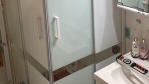 Un baño con cabina de ducha de vidrio, un lavamanos blanco y un espejo sobre él.