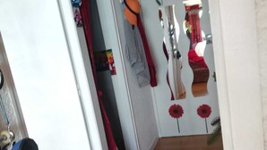 Un pasillo con piso de madera, una cortina roja y una puerta con un espejo que refleja una habitación con una cama y una decoración floral roja.