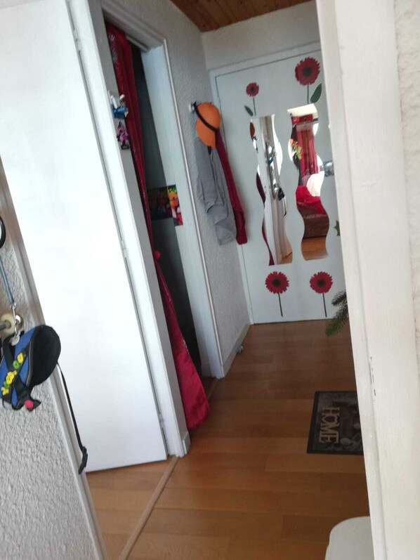 Un pasillo con piso de madera, una cortina roja y una puerta con un espejo que refleja una habitación con una cama y una decoración floral roja.