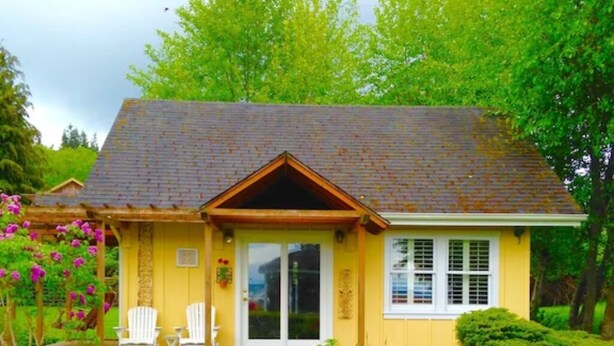 A yellow house with a porch, two white chairs, and a garden with various flowers. - It's Another Beautiful Day At Captain's Cove in Langley, On Whidbey Island (Langley)